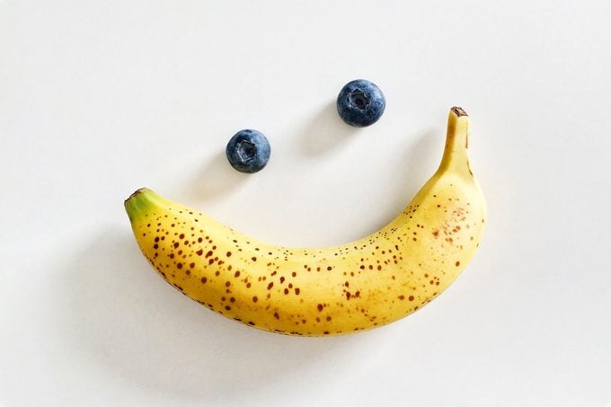 banana and two blueberries arranged to create the appearance of eyes and a smile on a white background