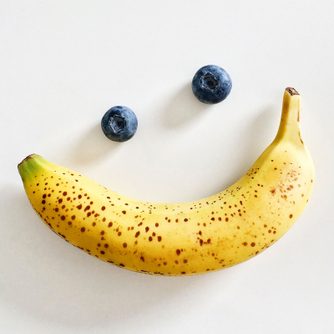 banana and two blueberries arranged to create the appearance of eyes and a smile on a white background