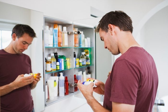 Man looking at bottles from medicine cabinet in bathroom
