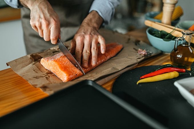 Young man cuts fresh salmon in kitchen to prepare a meal