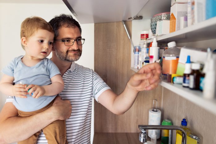 man holding his son while grabbing something from the medicine cabinet at home