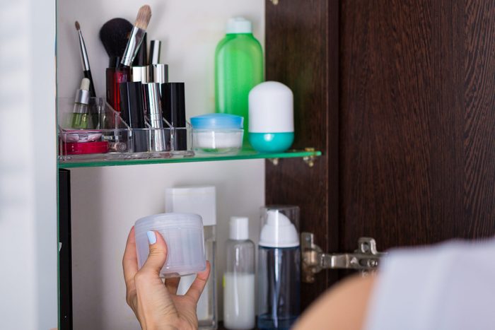 woman grabbing a product from medicine cabinet in bathroom
