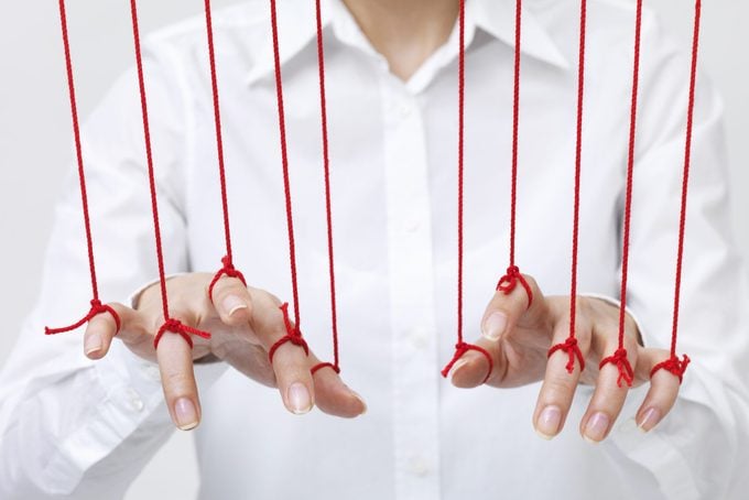 anonymous woman holding out her hands with her fingers being manipulated by red threads tied to each