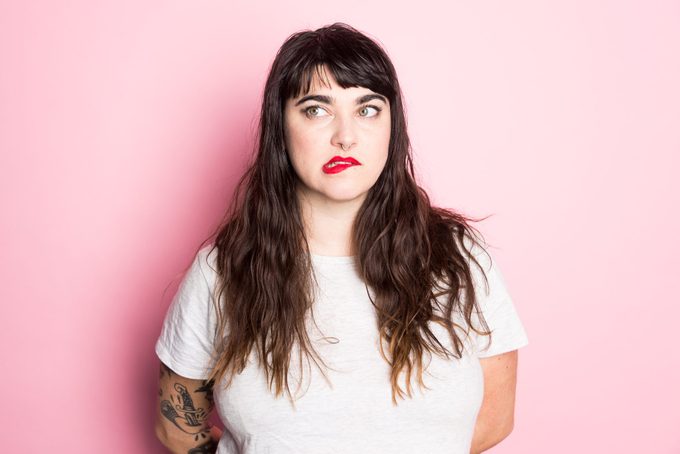 Portrait of a Woman with tattoos and red lipstick against a pink background