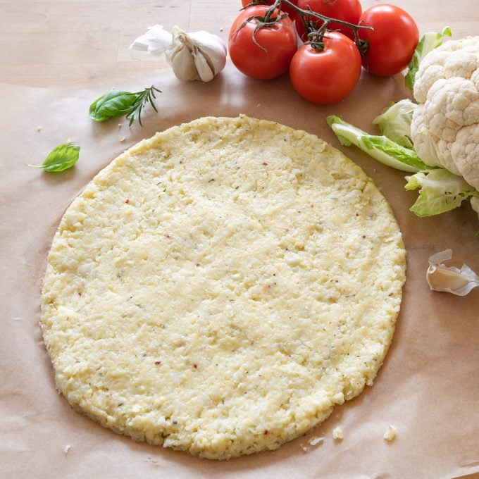 rohe Pizzabasis aus geriebenem Blumenkohl auf Backpapier, gesunde Gemüsealternative für kohlenhydratarme und ketogene Ernährung, Kopierraum