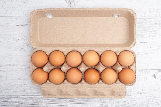 Dozen eggs in open cardboard packaging on white wooden table - top view with copy space