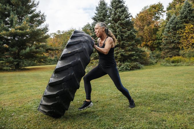 Mujer fuerte presionando neumáticos mientras hace ejercicio en el patio trasero