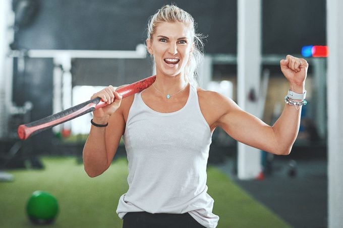 Portrait of a young woman cheering while holding a sledgehammer in a gym
