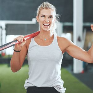 Portrait of a young woman cheering while holding a sledgehammer in a gym