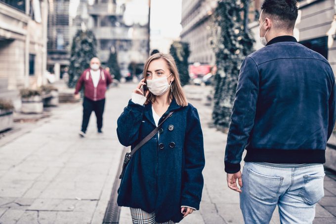 Female With Face Mask Talking On Smartphone While Walking In City And Protected Against COVID-19