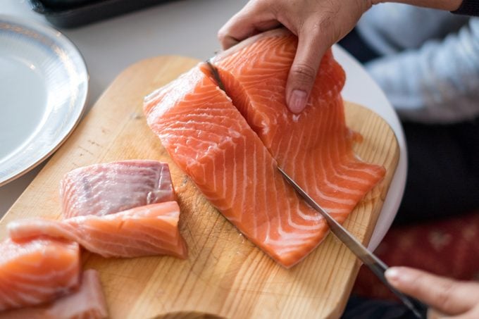 Hand chef using knife slice raw salmon on chopping board