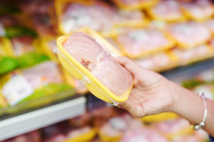 hand holding a package of raw chicken In a grocery store