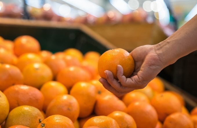 anonymous man chooses oranges in the supermarket.
