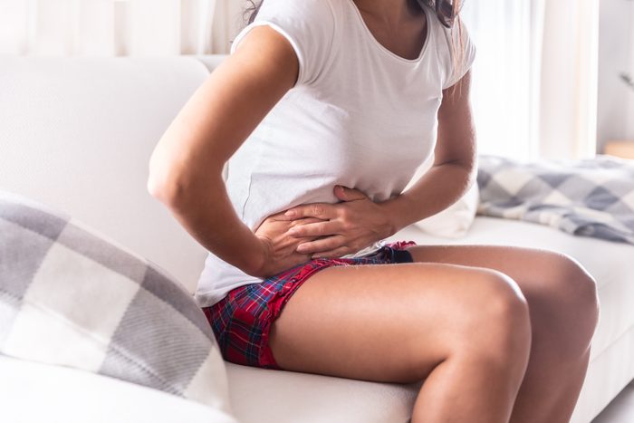Woman sitting on a couch at home holding her appendix in a stomach ache.