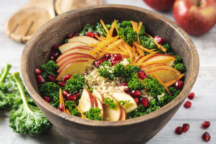 Kale salad with quinoa, apples, carrots and pomegranate seeds in wooden bowl