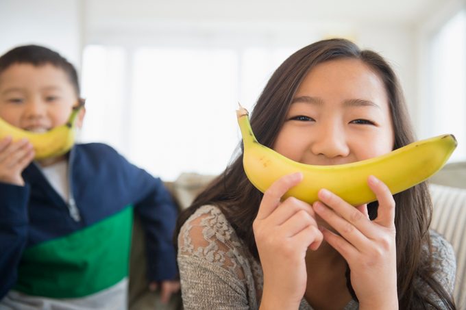 Kinder, die zum Lächeln Bananen vor Gesichter halten