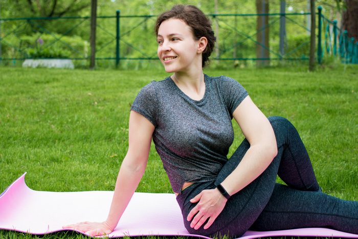 woman outside on a pink yoga mat does bone strengthening yoga pose, straight-legged twist