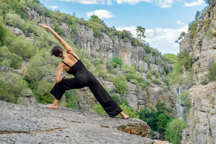 woman outside on cliff with view does a bone strengthening yoga pose, side angle pose