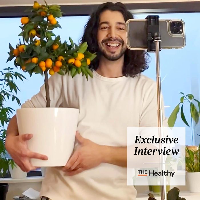 Tiktok Influencer Armen Adamjan holding a potted orange plant while filming with his phone on a table tripod