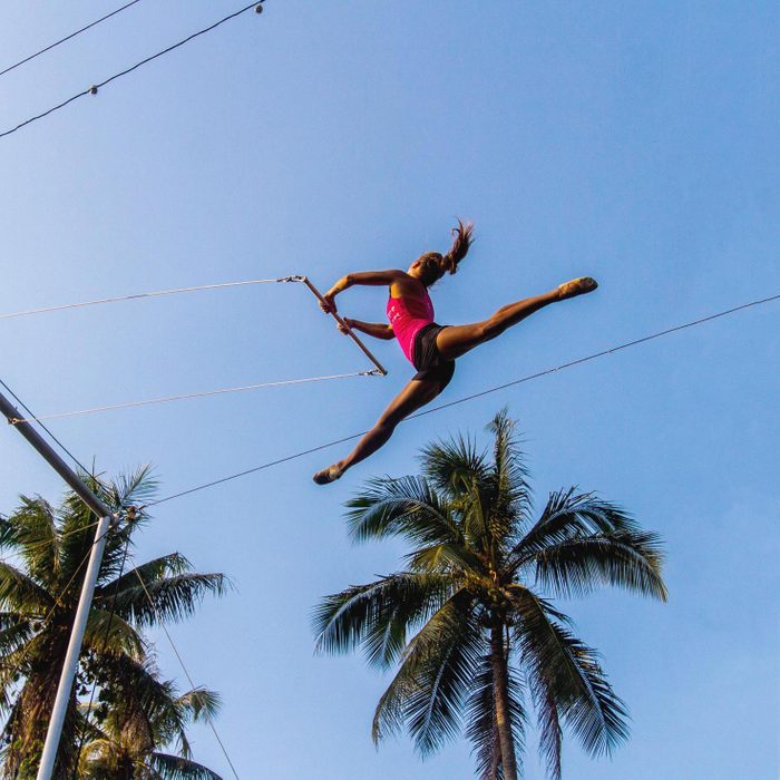 looking up at a woman doing the trapeze high in the sky surrounded by palm trees