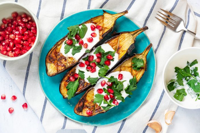 Grilled eggplant with yogurt, parsley, garlic and pomegranate on a blue ceramic plate