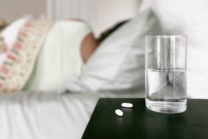 water and sleeping pills next to a bed with a sleeping woman in the background