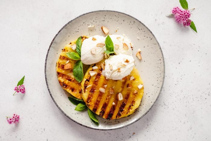 grilled pineapple slices on a plate with vanilla ice cream and topped with nuts