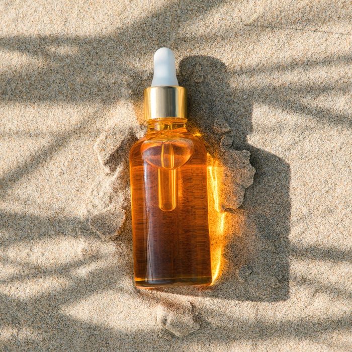 Golden orange bottle of sunburn oil or serum, moisturizer, sunscreen on sand background with hard shadow. Top view. Flat lay.