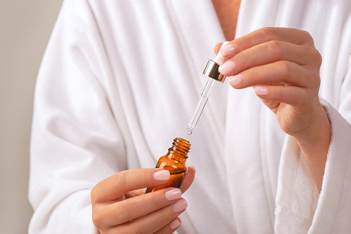 Woman in white bathrobe holds Beauty Product Facial Serum.