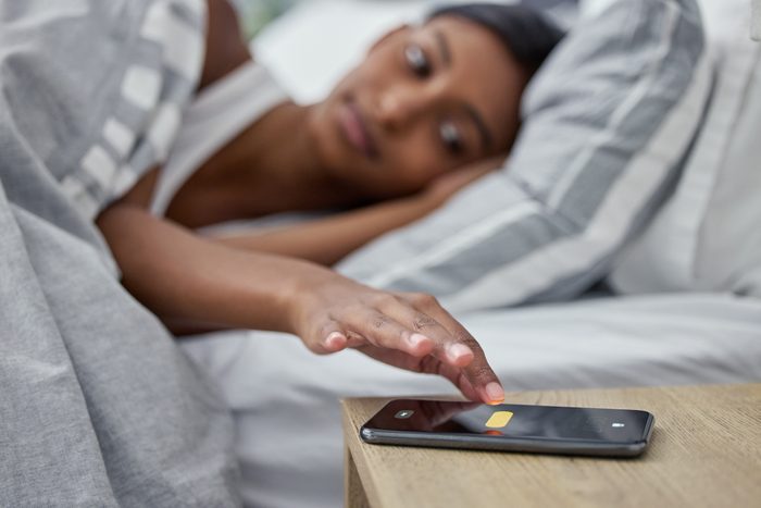 woman's alarm on her cellphone going off while she lies in bed