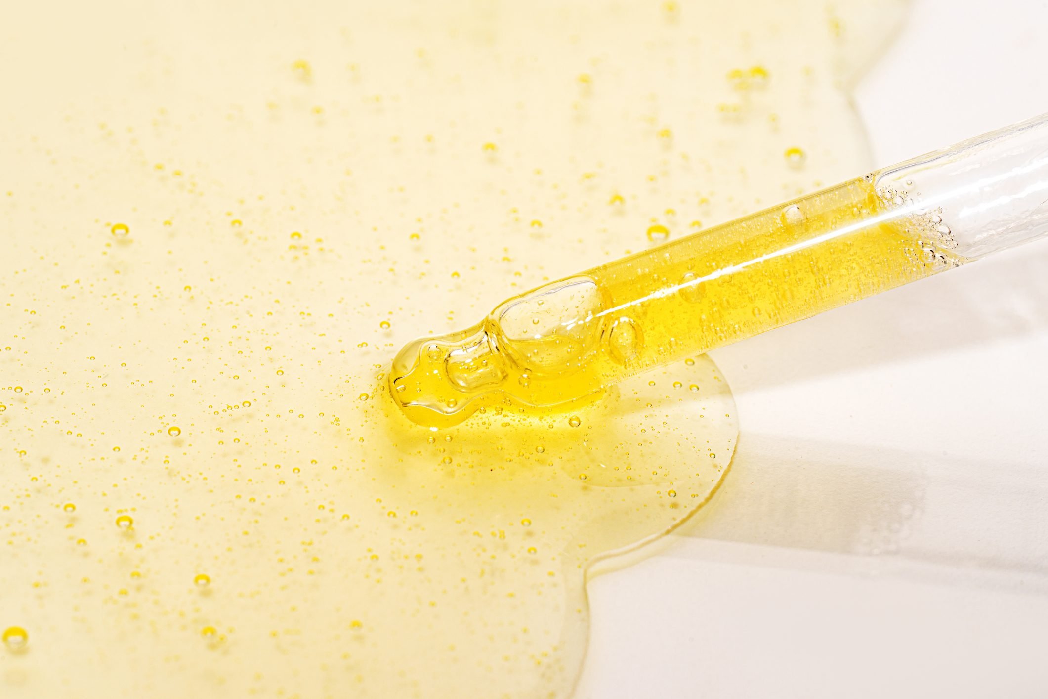 Close-up pipette with Face Serum or Essential Oil with Oxygen Aqua Bubbles on pastel yellow orange color background.