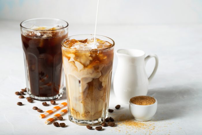 Ice coffee in a tall glass with cream poured over and coffee beans. Cold summer drink on a light blue background