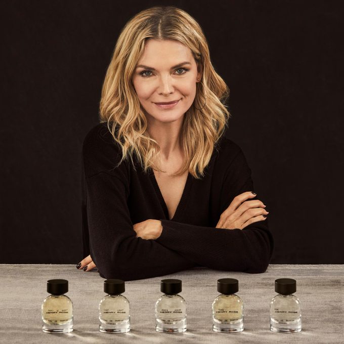 Retrato de Michelle Pheiffe en un suéter negro con botellas de perfume