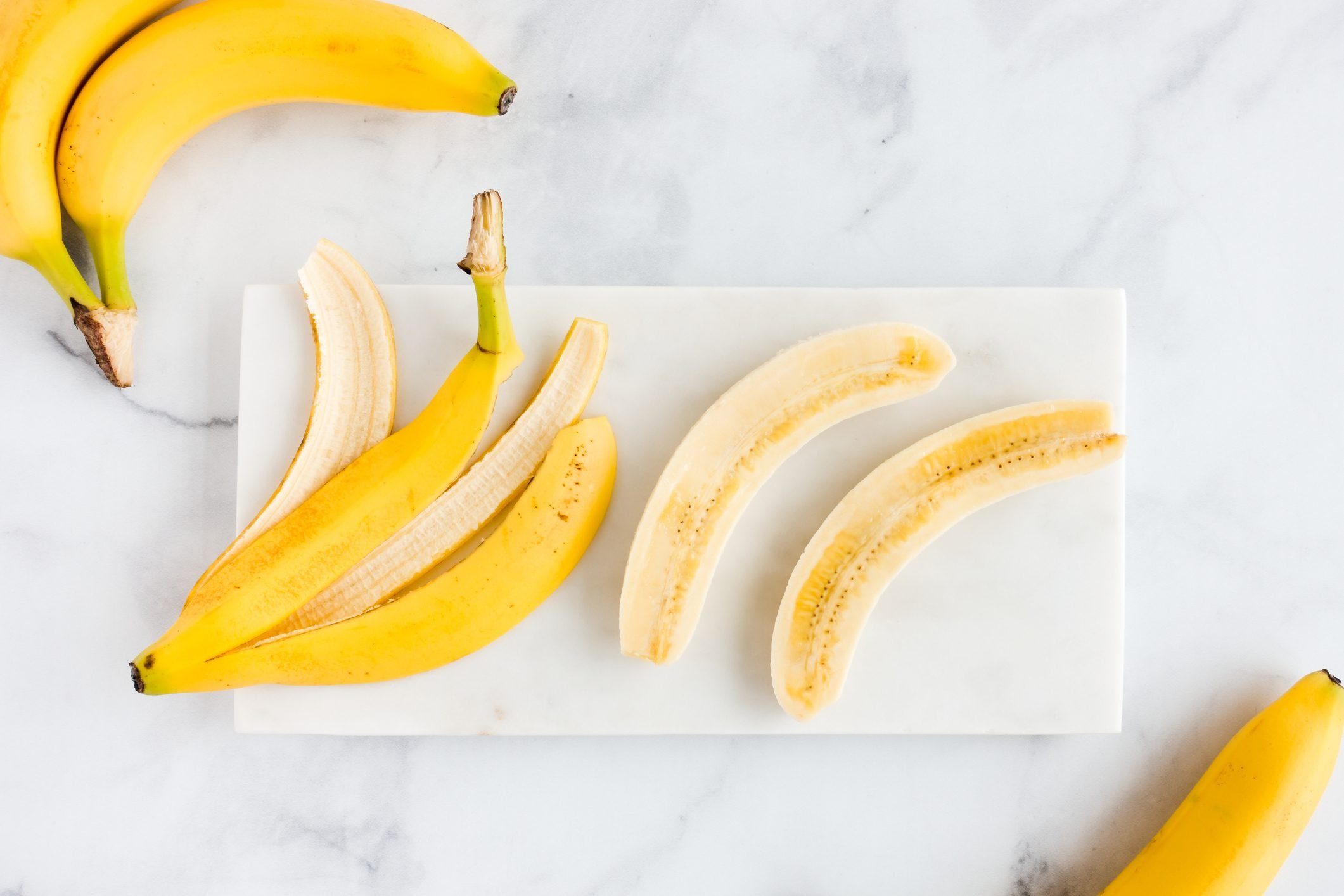 Banana Peel And Bananas On White Marble Board|tray with breakfast foods, including bananas, french toast, and coffee, on a bed with white sheets; a dog sits next to the tray
