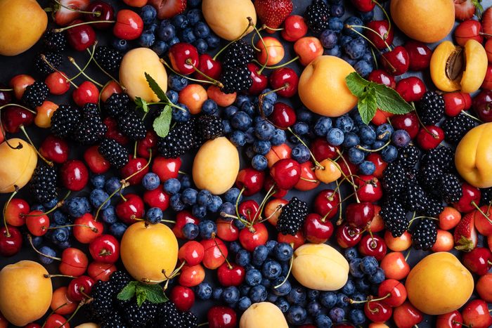 Fresh summer berry fruit colorful background. Sweet cherries, apricots, blackberries, blueberries, strawberries on grey background viewed from above, full frame