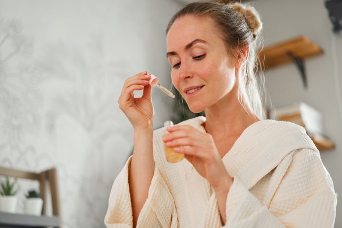 Smiling young female in bathrobe holding dropper of niacinamide