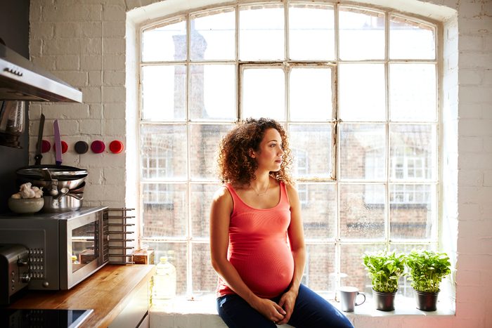 A pregnant woman sits in her kitchen window