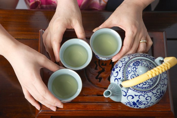 close-up of three hands holding small cups of tea