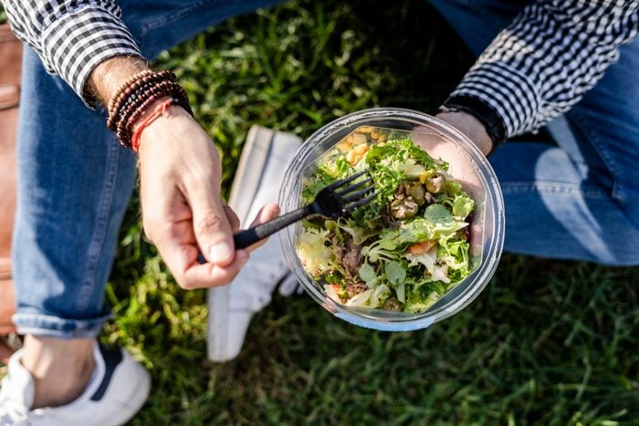 anonymous man sitting on grass eating mixed salad, partial view