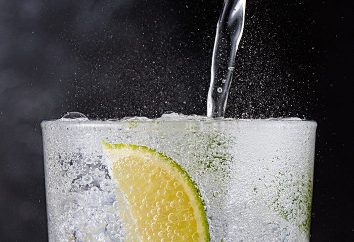 close up of a clear fizzy beverage on ice with a lime in the glass