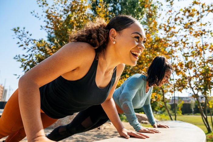 Cheerful women doing push-ups on retaining wall at park