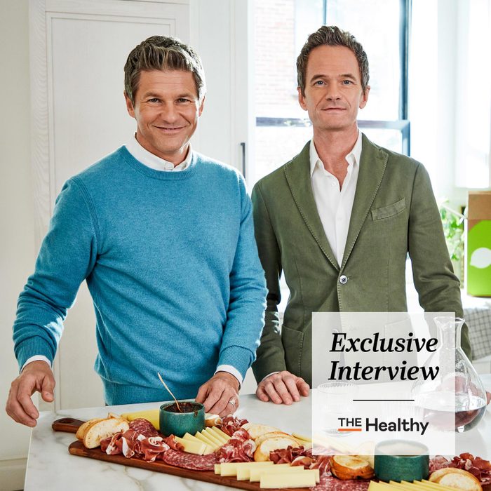 Neil Patrick Harris and David Burtka in the kitchen with a charcuterie board and The Healthy Exclusive Interview Logo in the corner