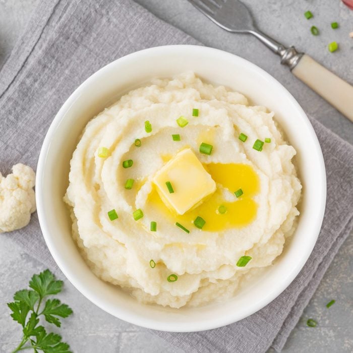 Cauliflower puree with butter and green onions in a white bowl on a gray concrete background. Healthy food