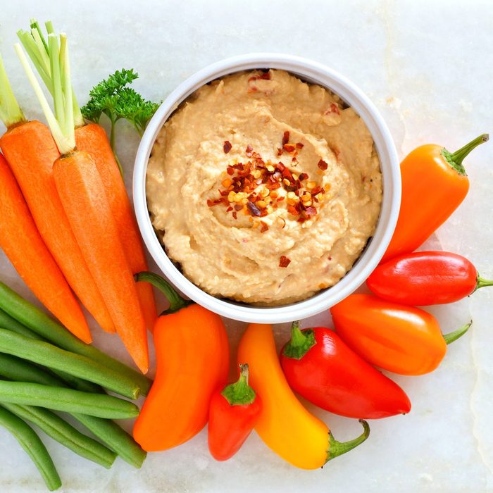Hummus with fresh vegetables, above view on white marble