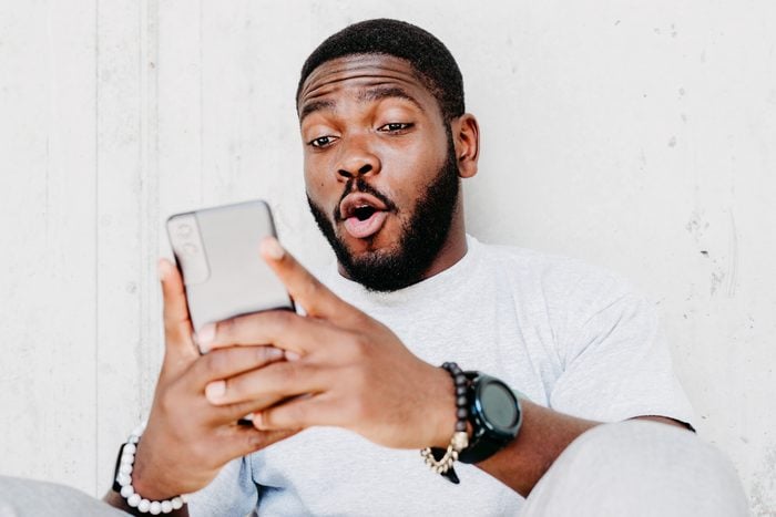 Young african american man with surprised facial expression hold smartphone in his hands