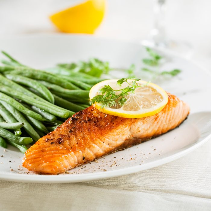 grilled salmon on a plate topped with lemon with a side of green beans