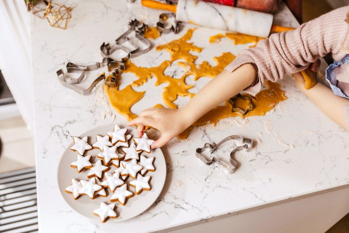 Close-up of girl taking Christmas cookie from plate on kitchencounter