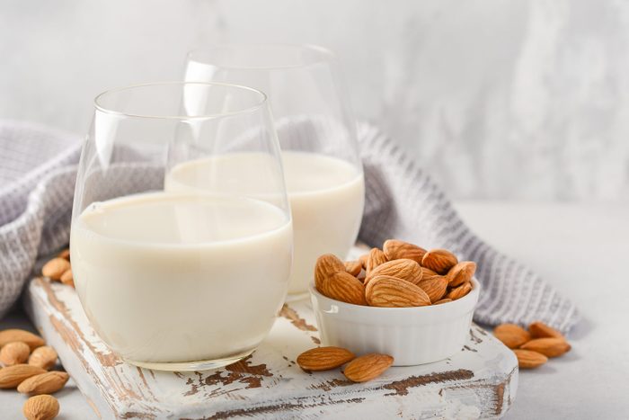 Almond milk and almonds on a white wooden cutting board.