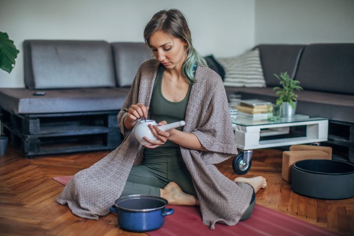 a woman sitting on the floor with a blanket preparing a neti pot