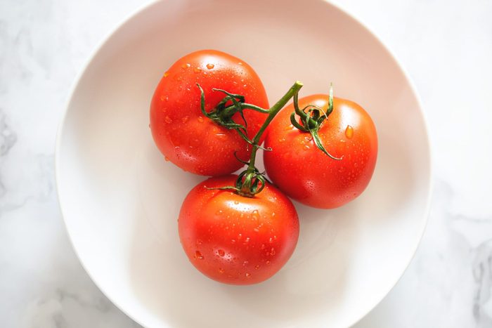 Three ripe red tomatoes on the vine shot in a brightly lit neutral setting.